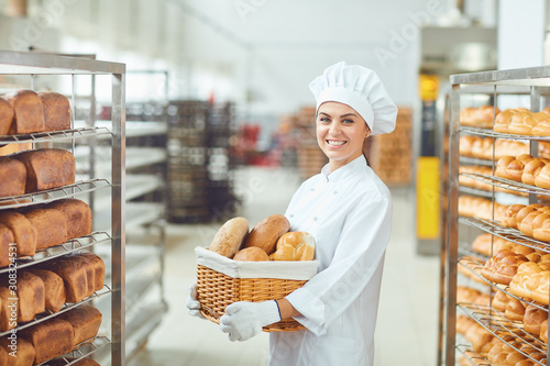 A baker woman holding a basket of baked in her hands at the bakery Fototapet