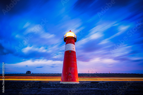 Traditional red and white colored lighthouse against twilight along the Dutch coastline at night