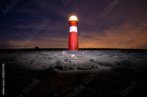 Traditional red and white colored lighthouse against twilight along the Dutch coastline at night