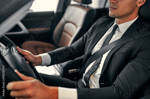 Cropped image of young handsome businessman is sitting in luxury car. Serious man in suit is driving. © Valerii Apetroaiei