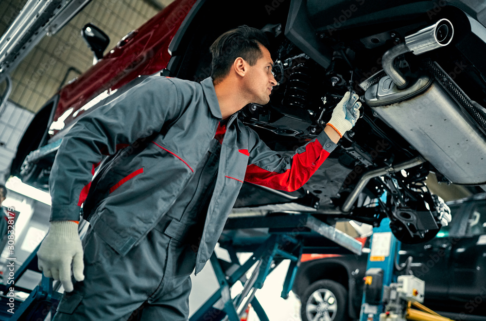 Handsome mechanic in uniform is working in auto service. Car repair and maintenance. Handsome mechanic in uniform is working in auto service. Car repair and maintenance.