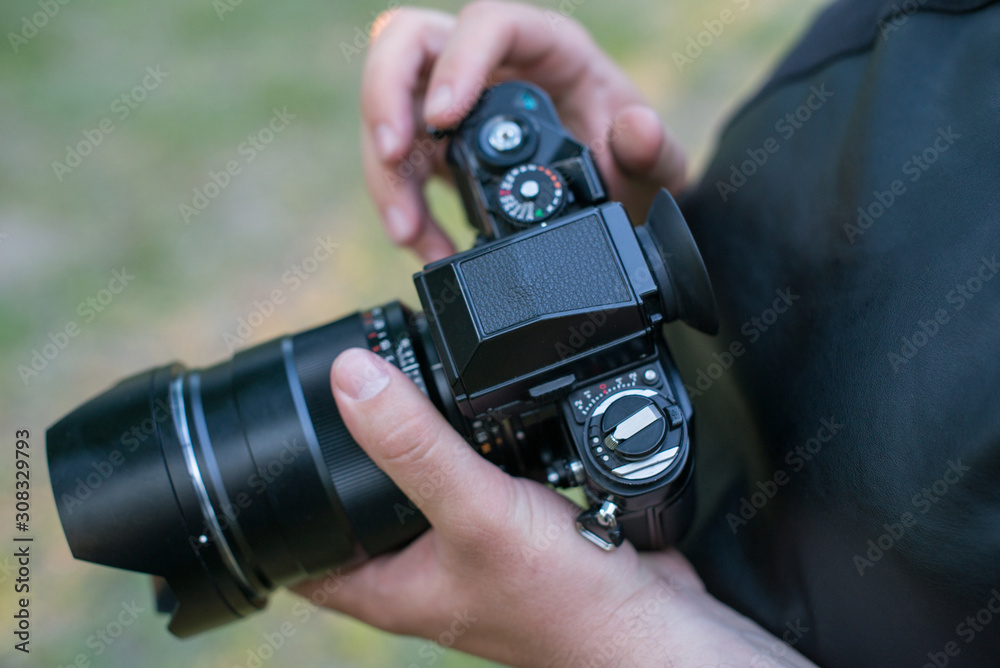 Closeup of a black camera holding by man's hand with natrural blackground in sunny day.
