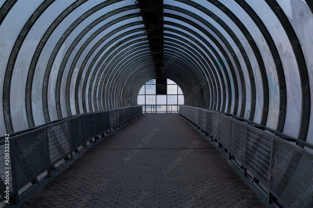 A long pedestrian tunnel with metal arches and glass design. Aerial pedestrian crossing over the highway, a dark empty tunnel no people