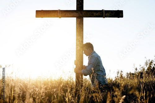 Foto Male with his head leaned against a hand made wooden cross while praying