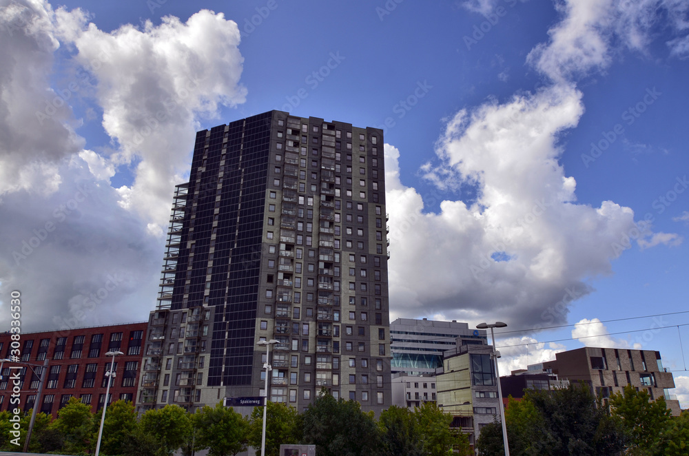 Amsterdam, Holland, August 2019. In the modern periphery of the city a building with a large roof with photovoltaic panels. The facade is characterized by verandas balconies and photovoltaic panels Amsterdam, Holland, August 2019. In the modern periphery of the city a building with a large roof with photovoltaic panels. The facade is characterized by verandas balconies and photovoltaic panels