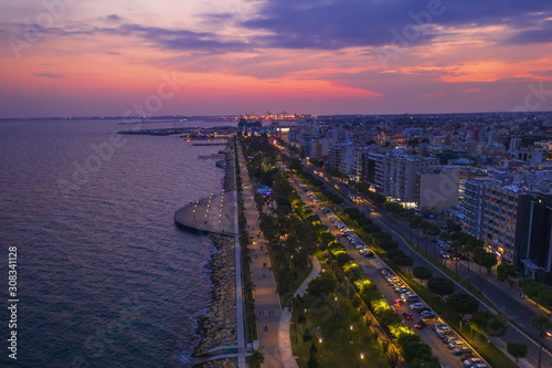Limassol, Cyprus, aerial panoramic view at promenade or embankment at evening after sunset. Famous Limassol walking alley with evening illumination, palms and wooden piers in resort town, drone photo.