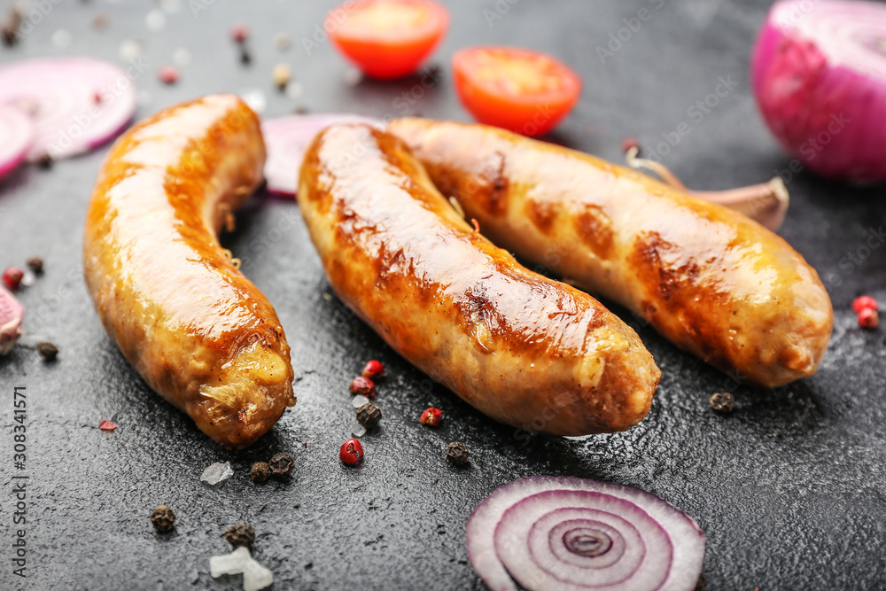 Tasty grilled sausages with vegetables and spices on dark background Tasty grilled sausages with vegetables and spices on dark background