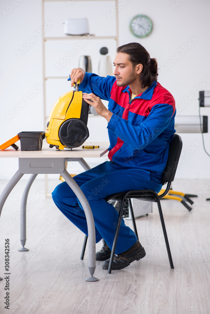 Young male contractor repairing vacuum cleaner at workshop Young male contractor repairing vacuum cleaner at workshop