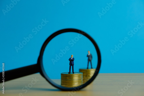 Miniature people business concept - a businessman standing on coin stack with magnifier, searching for financial solution / strategy