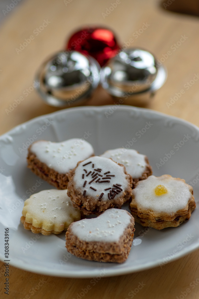 Jam and cream filled cookies with sugar sweet white icing on white plate on wooden table, group of Christmas sweets