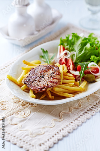 Grilled Steak with french fries and fresh salad. White wooden background.  