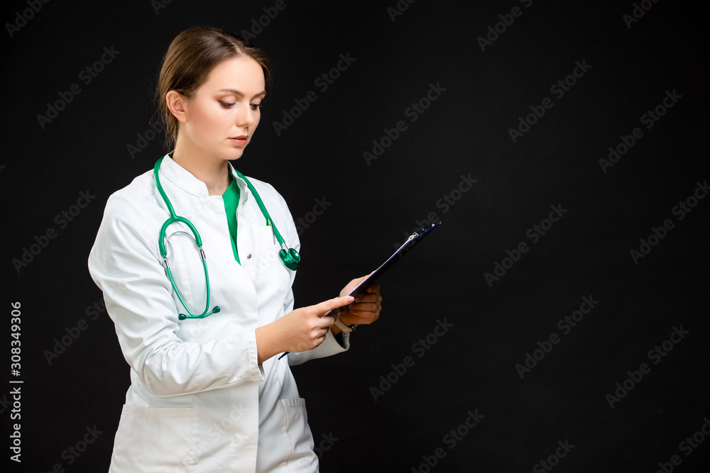 Medicine Concepts. Portrait of Professional Female GP Doctor Posing in Doctor's Smock and Endoscope. Reading Documents. Against Black.Horizontal Composition Medicine Concepts. Portrait of Professional Female GP Doctor Posing in Doctor's Smock and Endoscope. Reading Documents. Against Black.Horizontal Composition