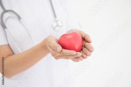 Young woman doctor holding a red heart, standing