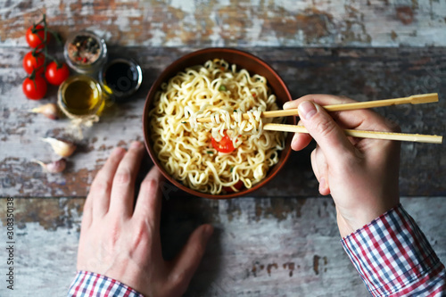 Selective focus. A man holds chopsticks with chinese noodles. Chinese noodle bowl with spices.