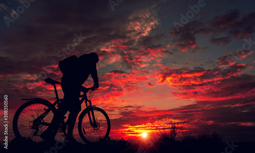 cyclist with a bicycle, in the background fiery sunset. © Lumppini