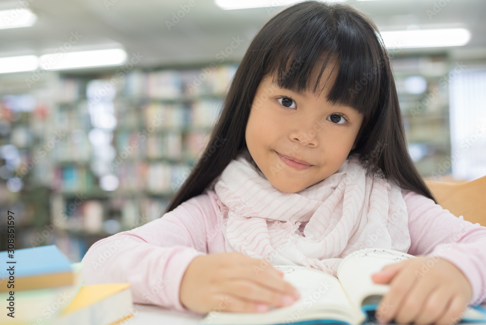 portrait of cute schoolgirl smiling while sitting with stack of books at table in library portrait of cute schoolgirl smiling while sitting with stack of books at table in library