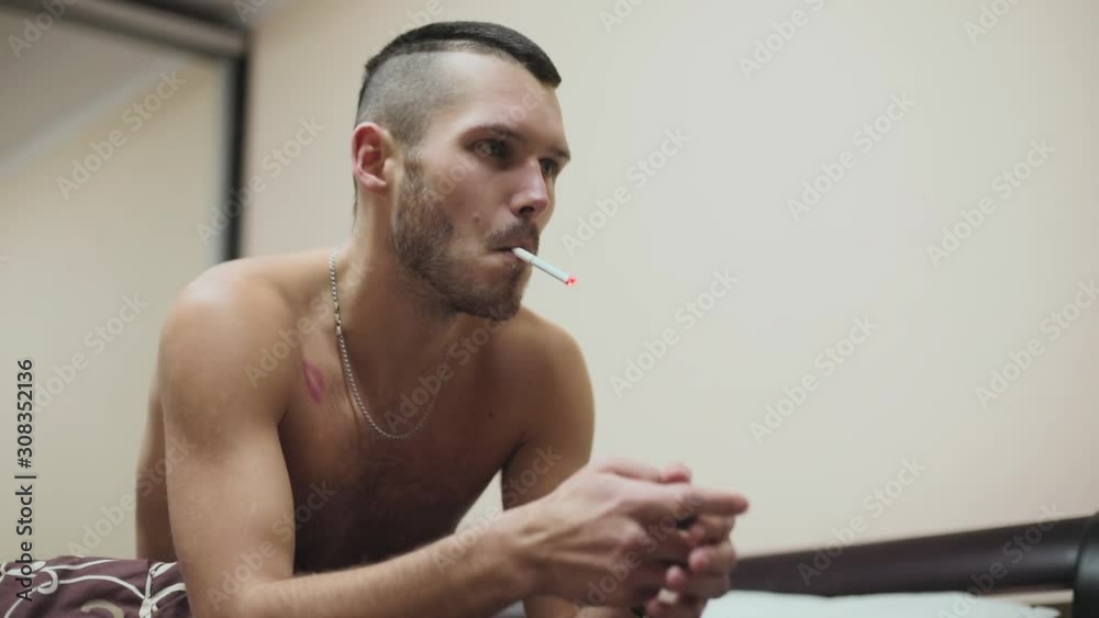 Close up serious topless good-looking fit young man smoking cigarette in bed at home bedroom tobacco guy handsome apartment slow motion