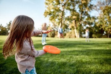 Making memories, breaking the distance. Little girl playing frisbee with her family in the park on a sunny day