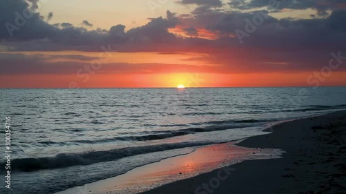 A beautiful full sunset over breaking ocean waves on Gulf of Mexico Florida beach on a vacation by the sea is featured in this one minute long video footage