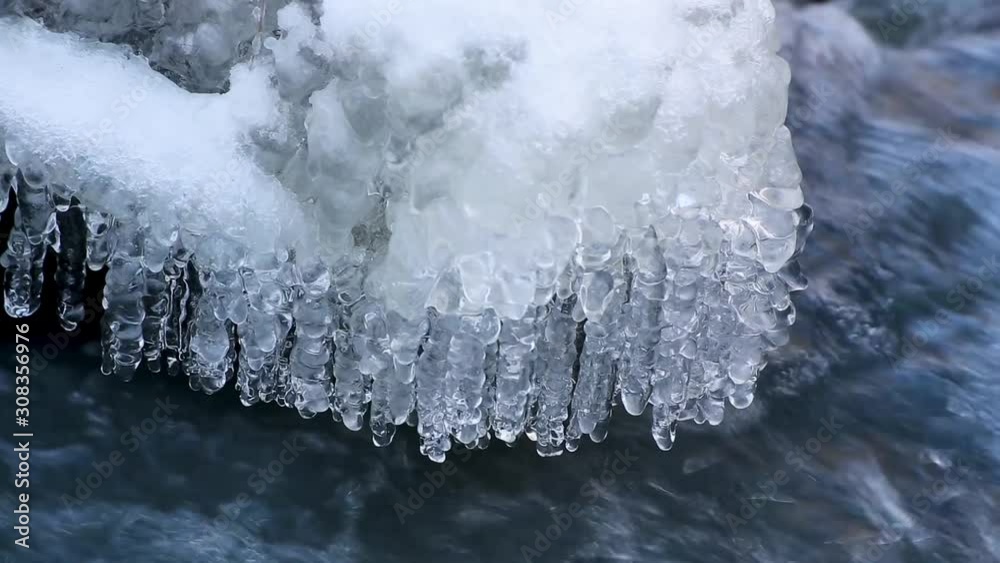 Seamless video loop features a snowy creek with flowing water and frozen icicles in winter weather