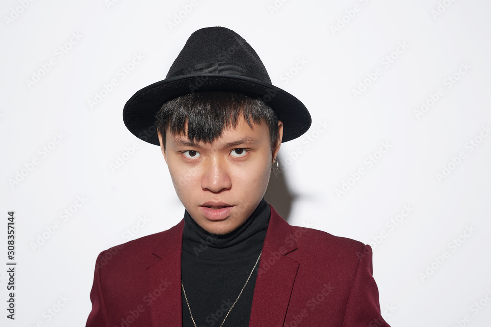 Head and shoulders portrait of fashionable Asian man wearing maroon suit and stylish hat while posing against white background at party, shot with flash Head and shoulders portrait of fashionable Asian man wearing maroon suit and stylish hat while posing against white background at party, shot with flash