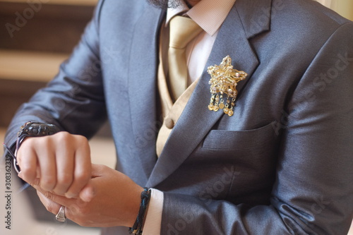 Man in dark grey suit two bottons golden star brooch, checking whatch, close up
