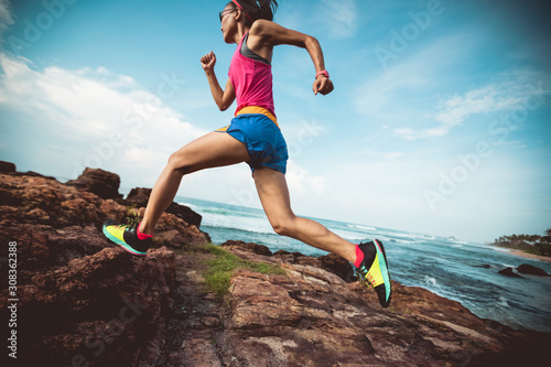 Young fitness woman trail runner running to rocky mountain top on seaside © lzf