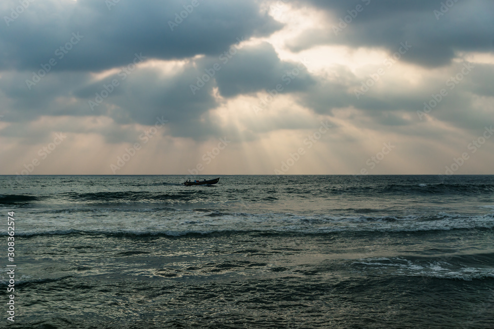 Fishing boat in the waves of the ocean with orange sun rays, Varkala, India