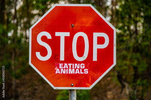 Landscape image of a tradional red traffic warning sign with humorous sustainability message 'STOP Eating Animals' to promote vegetarian and vegan lifestyle