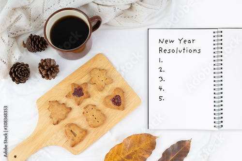 Hot cup of coffee with Christmas cookies and pine tree serve on white bed sheet in the morning top view with paper note writing of text new year 2020 resolutions.