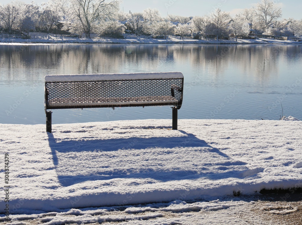 Steel bench covered by snow facing the pond on a beautiful winter morning
