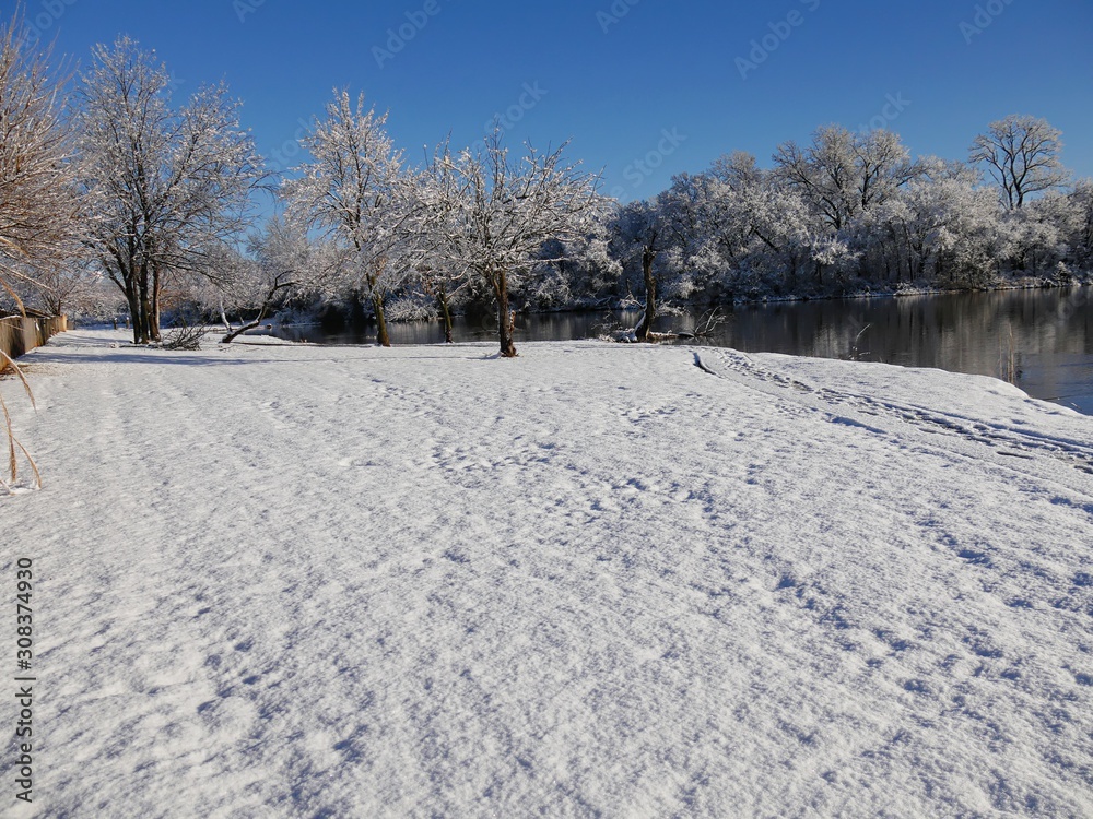 Wide scenic tranquil view of fresh white snow covering the ground by the pond Wide scenic tranquil view of fresh white snow covering the ground by the pond