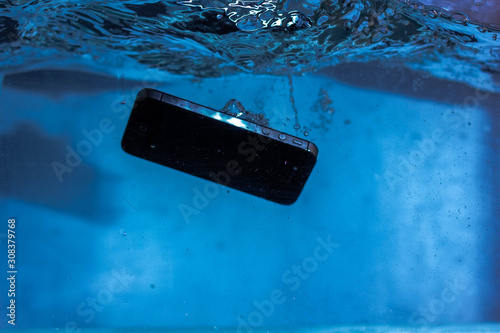 black and white phone dropped into the water. phone in water. blue water. phone in water bubbles.phone sinks in water photo