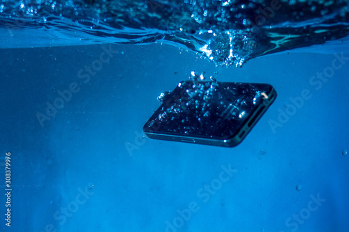 black and white phone dropped into the water. phone in water. blue water. phone in water bubbles.phone sinks in water