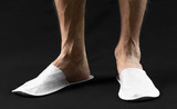 The feet of a man in white slippers. On black background. Close up