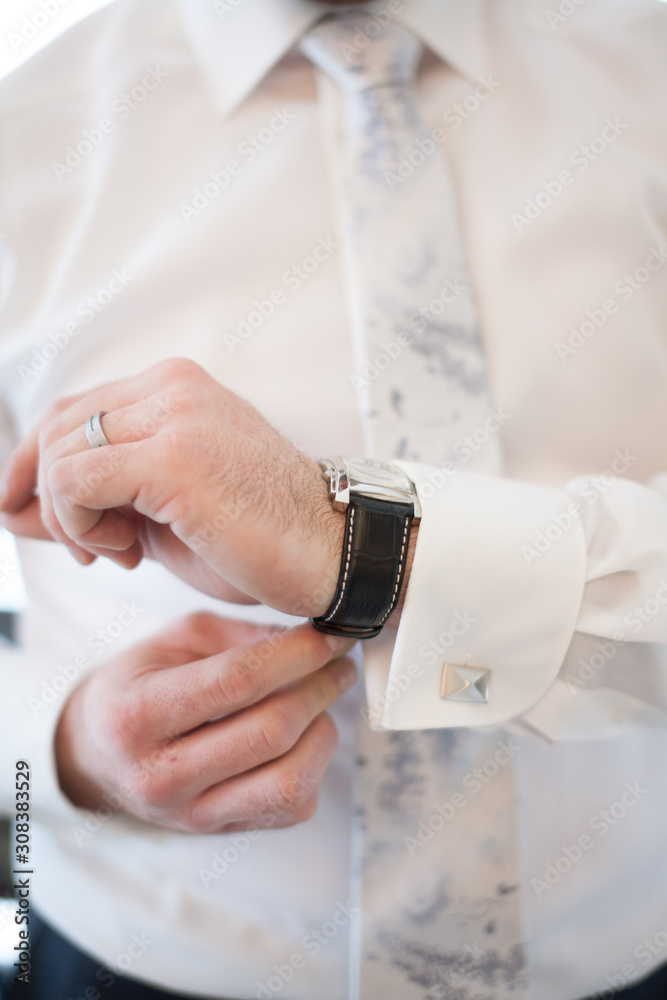 Elegant young fashion business man or groom looking at the cufflinks of his suit while fixing them Elegant young fashion business man or groom looking at the cufflinks of his suit while fixing them