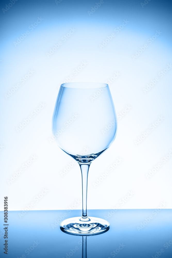 Red wine glass on the light background. Fine cristal glassware concept. Vertical, toned in blue Red wine glass on the light background. Fine cristal glassware concept. Vertical, toned in blue