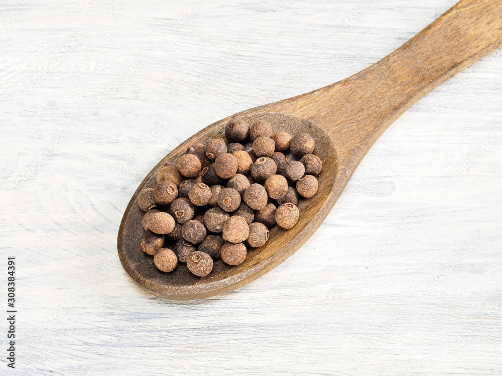 Allspice in wooden spoon on a white background. Indian cuisine, ayurveda, naturopathy, modern apothecary concept Allspice in wooden spoon on a white background. Indian cuisine, ayurveda, naturopathy, modern apothecary concept