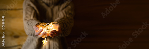 Female hands holding Christmas light decorations on wooden background. Xmas and New Year theme.