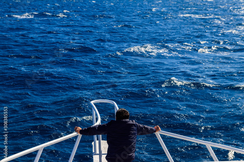 Man standing on the white bow of yacht and looking on sea or ocean. Luxury vacation concept. Back view