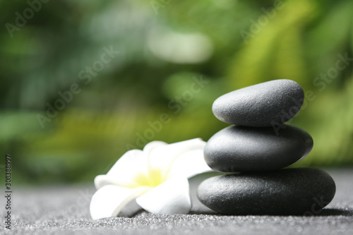 Stones and plumeria flower on black sand against blurred background. Zen concept