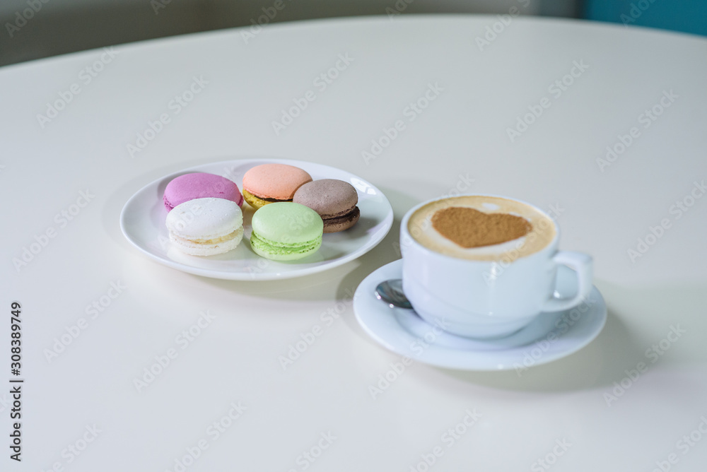Delicious macaroons and cappuccino on a large bright table in a cozy coffee shop Delicious macaroons and cappuccino on a large bright table in a cozy coffee shop
