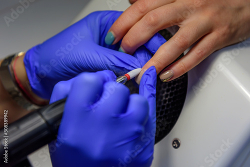 Process of cleaning the nail from old coating, preparing before applying nail polish. Manicure master makes a hardware manicure in blue gloves removing the gel polish in salon.