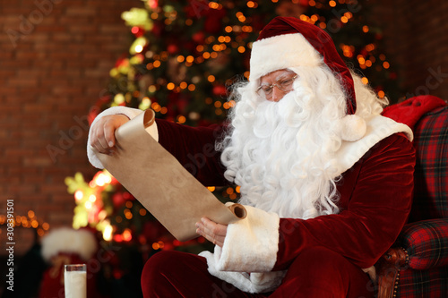 Santa Claus with wish list near Christmas tree indoors