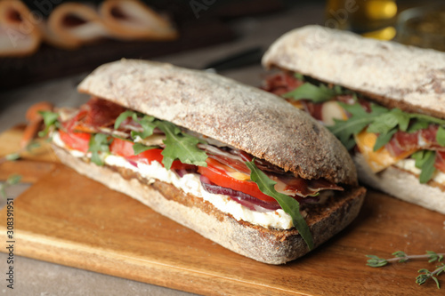 Delicious sandwiches with fresh vegetables and prosciutto on table, closeup photo