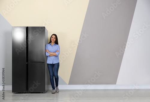 Happy young woman near refrigerator indoors, space for text