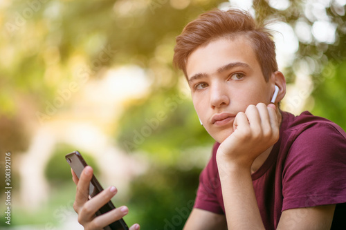 Close-up portrait of a thoughtful unhappy teenage boy with smartphone, outdoors Fototapeta