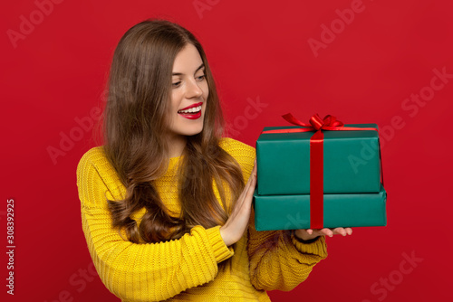 happy beautiful girl looking at Christmas presents isolated on red background, shows white teeth. Christmas concept