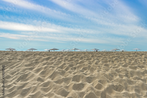 A baltic beach on a background of blue sky and white clouds. Umbrellas from the sun and the sea. Dune of white sand in the foreground.