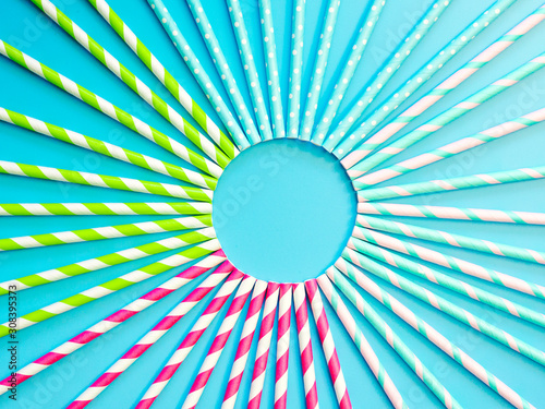Top-down view of colorful paper drinking straws on blue background. Copy space in center for text or design. Top view or flat lay.